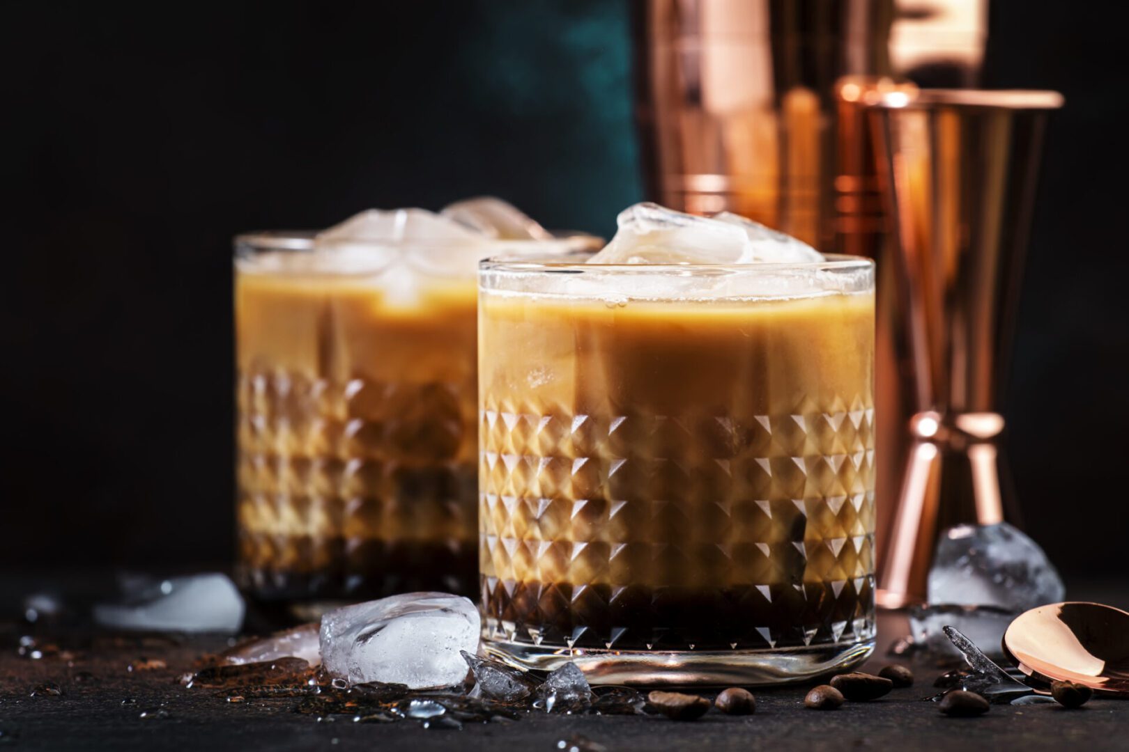 Two iced coffee drinks in textured glasses with ice cubes.