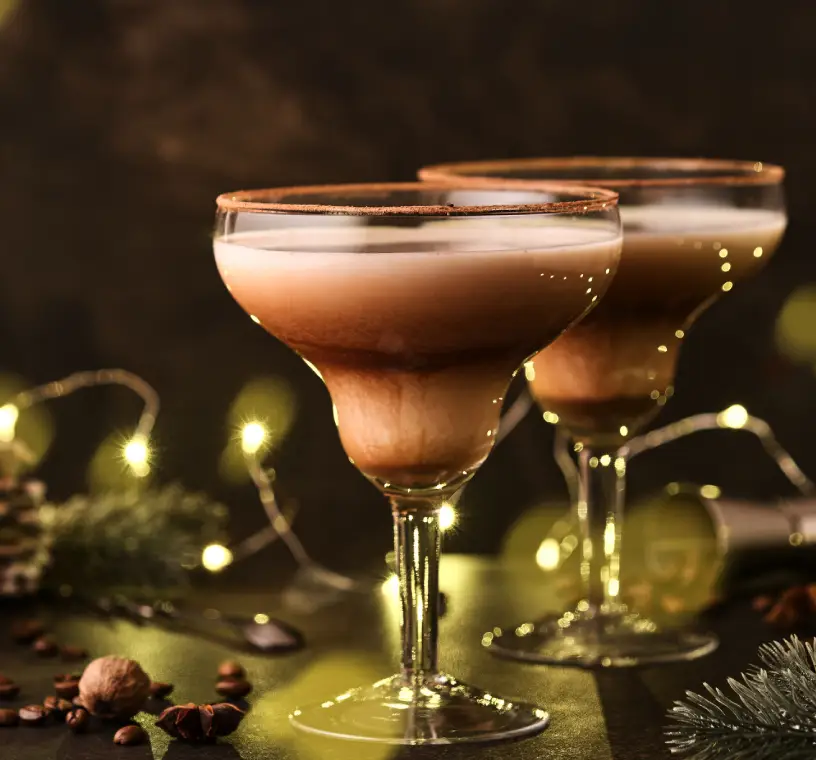 Two creamy chocolate cocktails in elegant glasses with festive lights.
